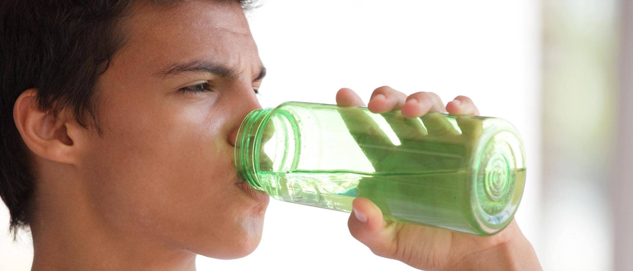 Teen drinks water from green bottle