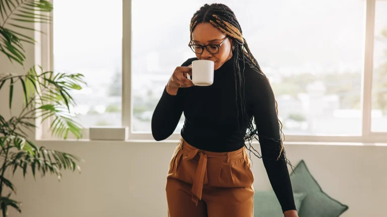 African American woman standing up and drinking coffee in the office