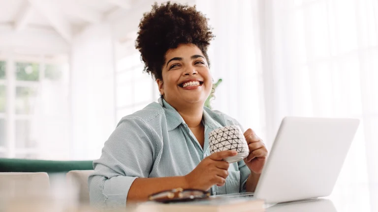 African American woman drinking coffee at her desk and smiling