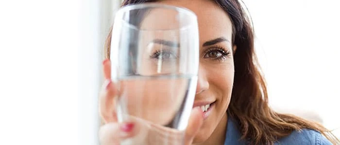 Woman holding a clear glass of water up to her eye and looking through the glass