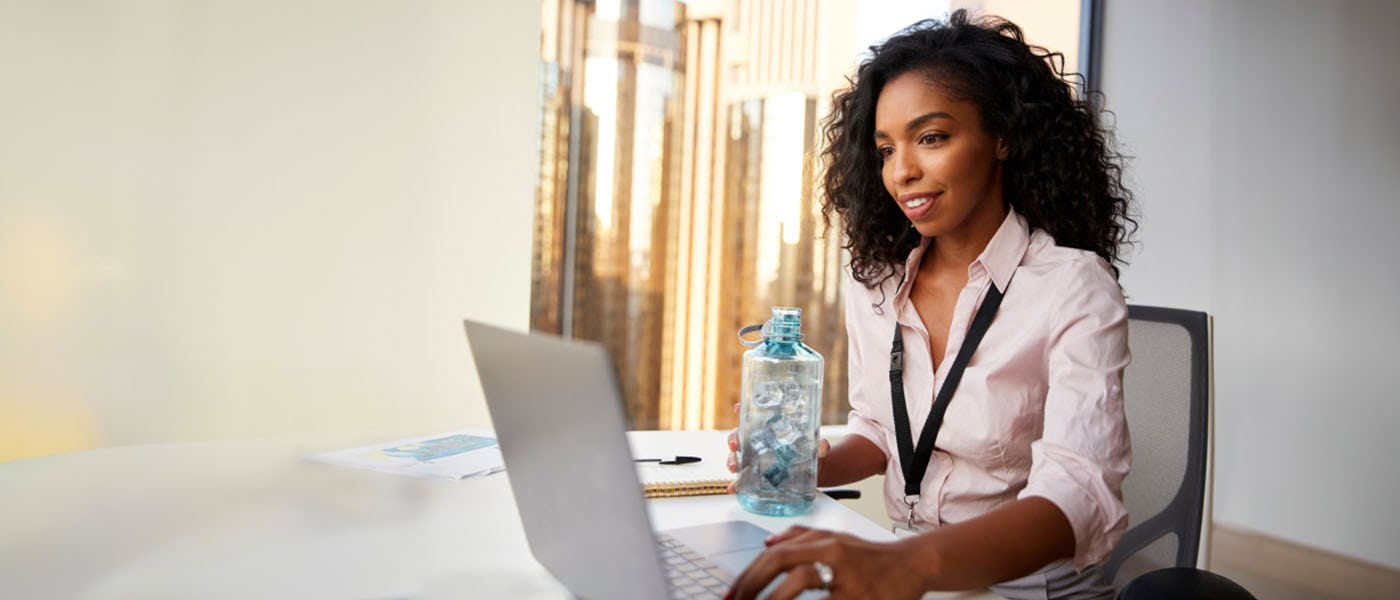 african american woman holding a blue bottle full of ice and looking at a laptop