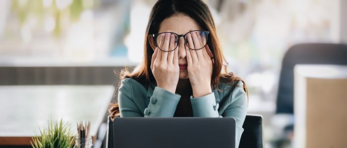 woman rubbing her eyes in front of computer