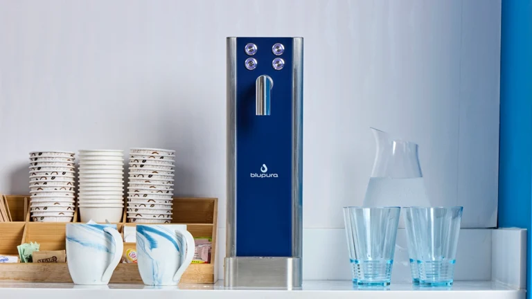 Quench 580 sparkling water dispenser on a counter with 2 mugs and 4 glasses next to it